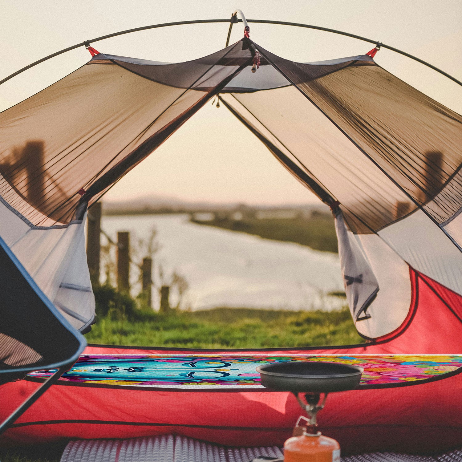 an image through a tent with camping mat and stove, with a lake in the backgorund