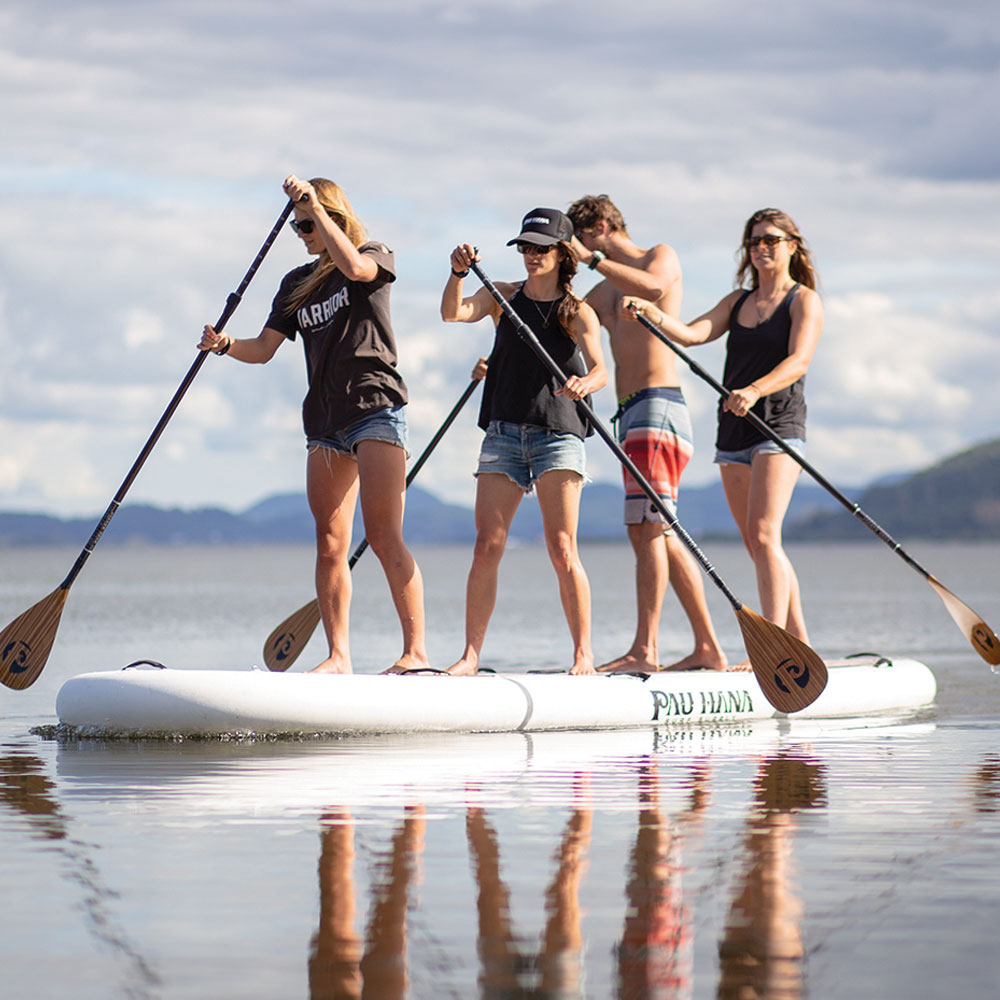 four people paddling the oahu nui giant inflatable paddleboard on a lake with mountains in the backgorund