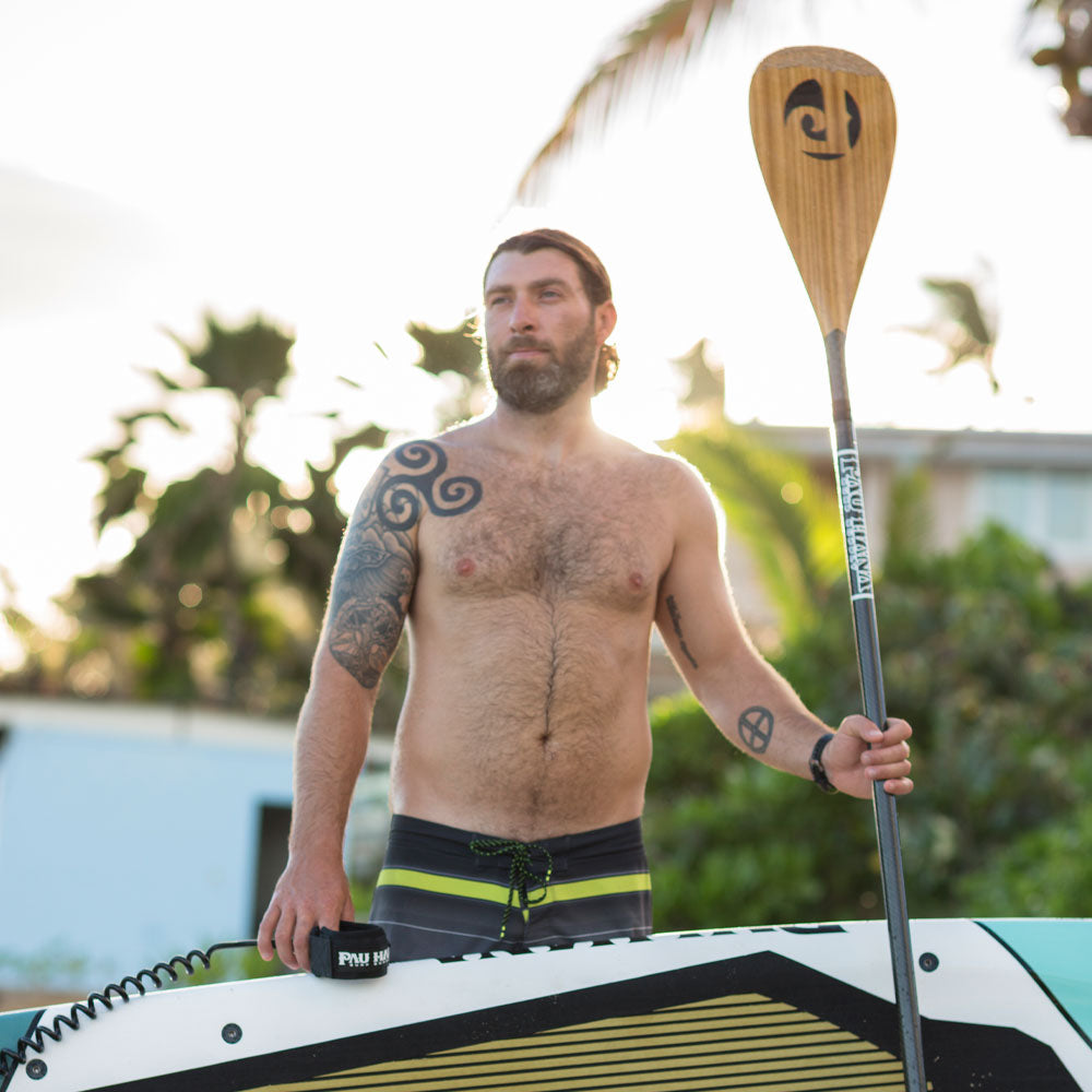 a man holding the carbon teak sup paddle standing next to a paddleboard