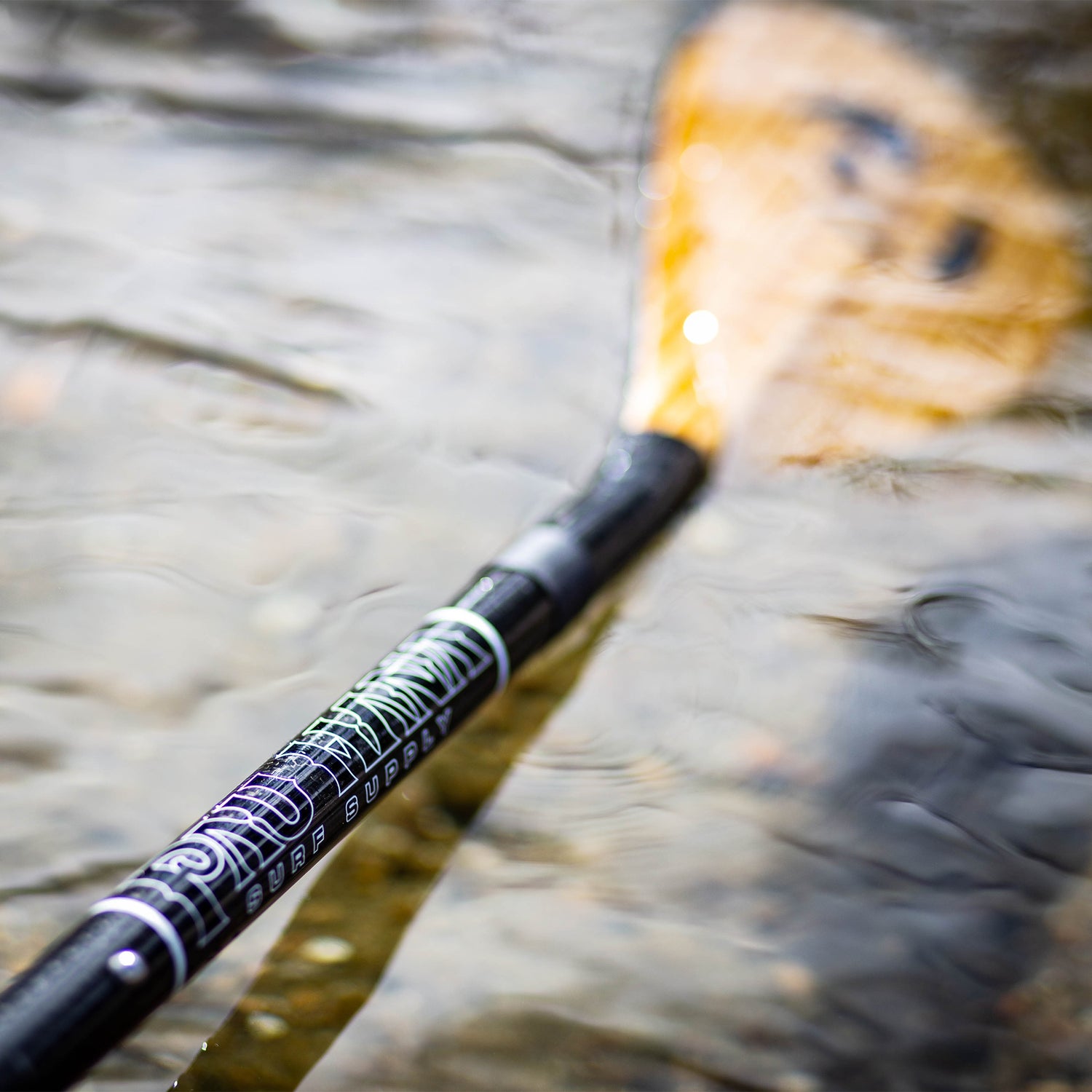 a close up of the pau hana carbon teak sup paddle in the water