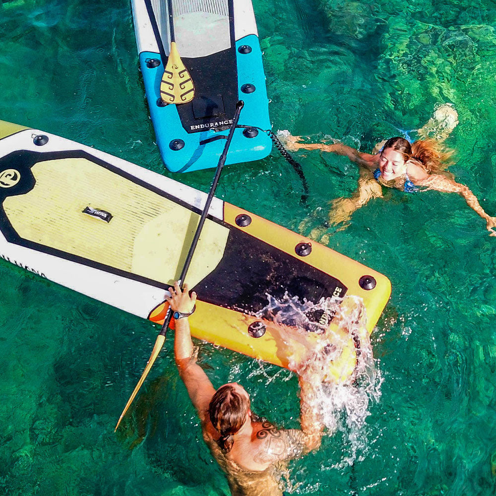 a couple swimming in the blue sea next to inflatable paddleboards having fun
