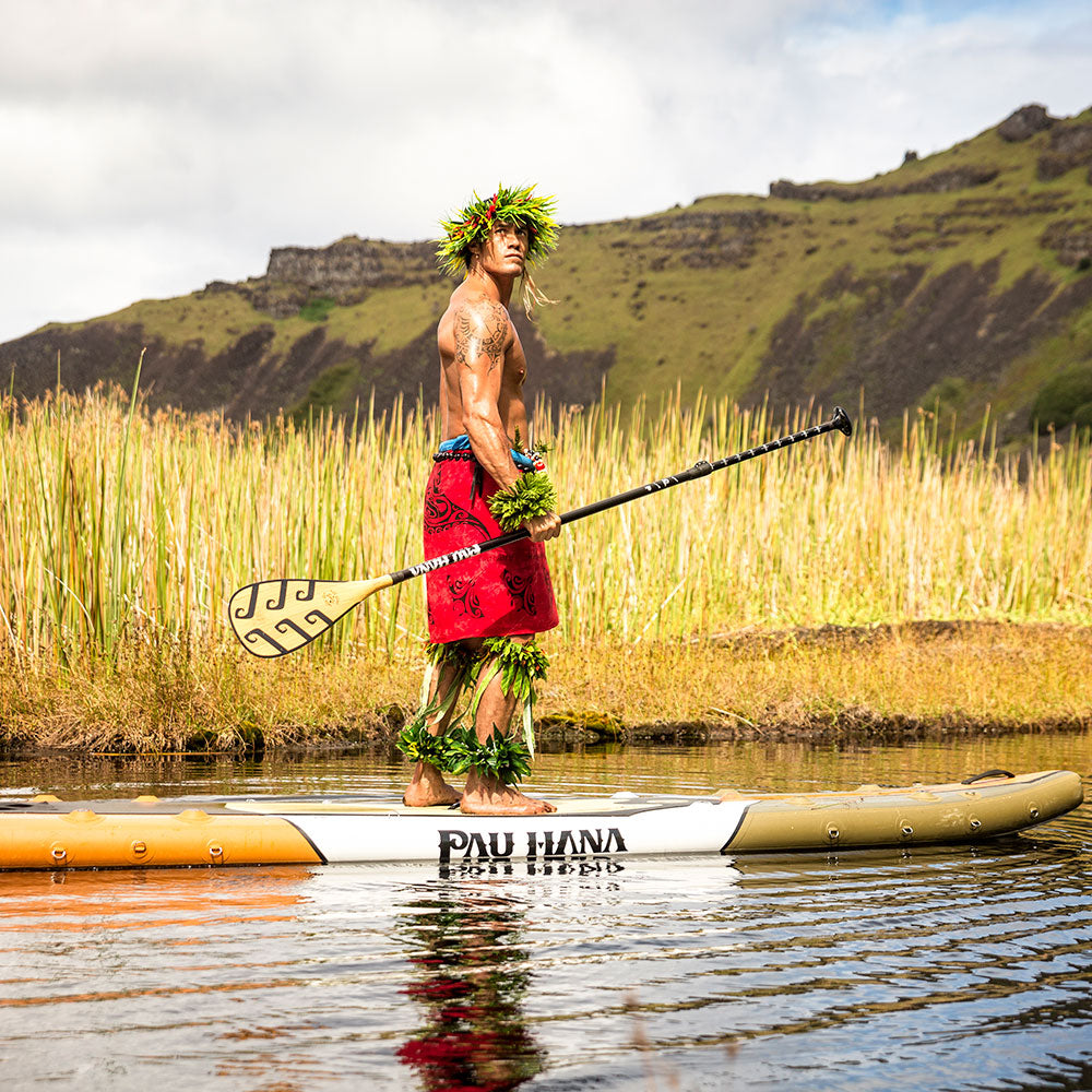 a native paddling on a lake with the endurance sup inflatable paddle board with tall grass and hills in the background