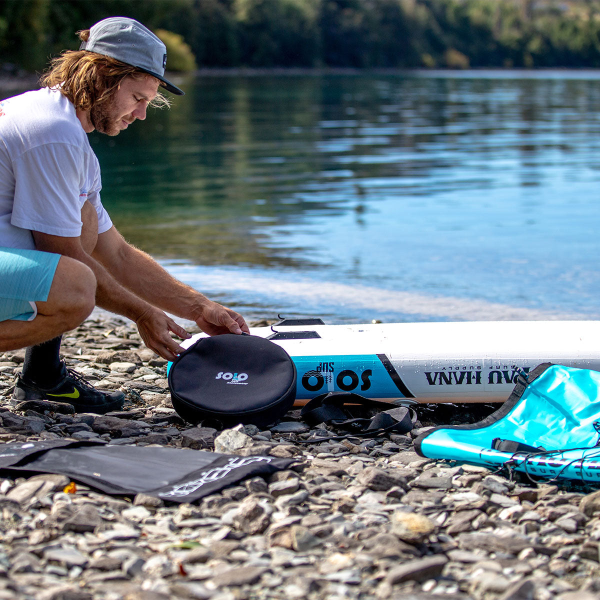 a person setting up an infalatable paddlboard on a pebble beach in new zealand