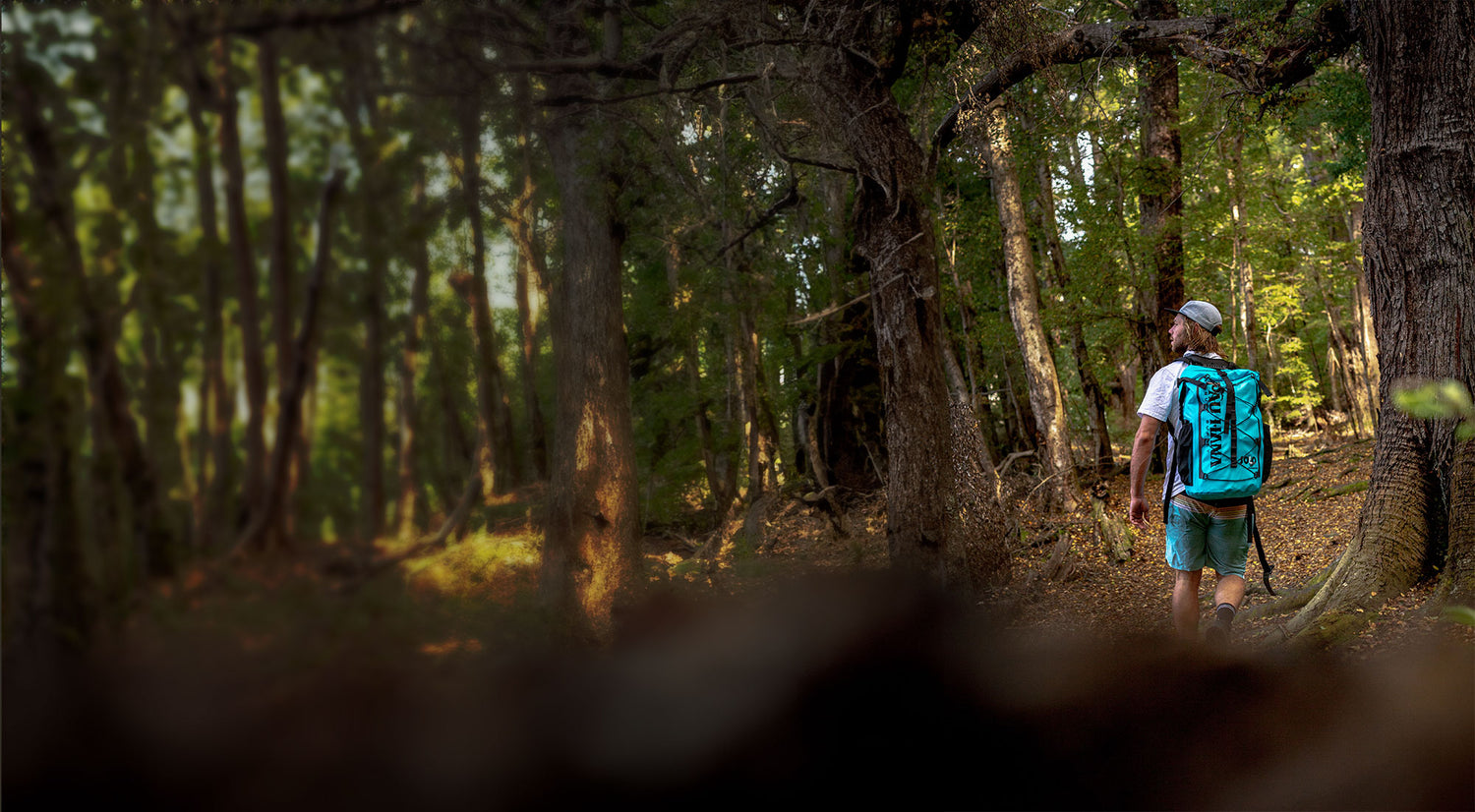 a man hiking through the forest with the solo sup backcountry inflatable paddleboard backpack on his back