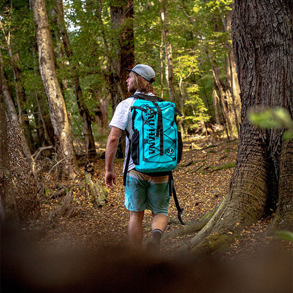 a man walking through the forest with a stand up paddlebaord in a backpack