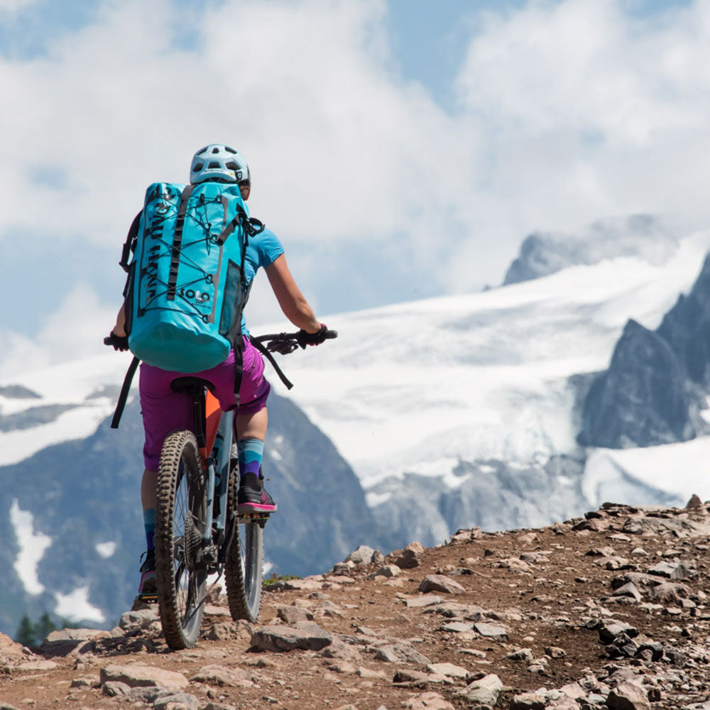 a person biking with the solo sup backcountry backpack with mountains in the background