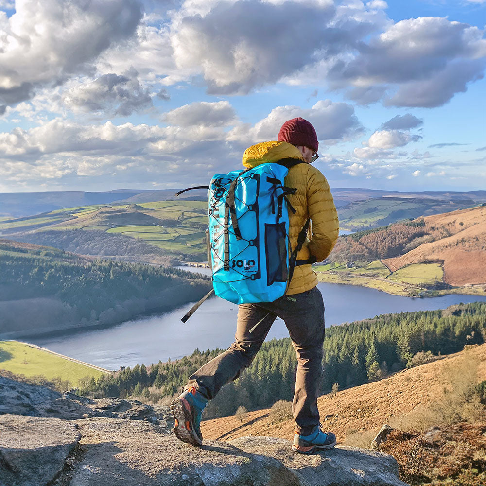a man walking through the british hills wearign the solo sup backpack with a lake in the background