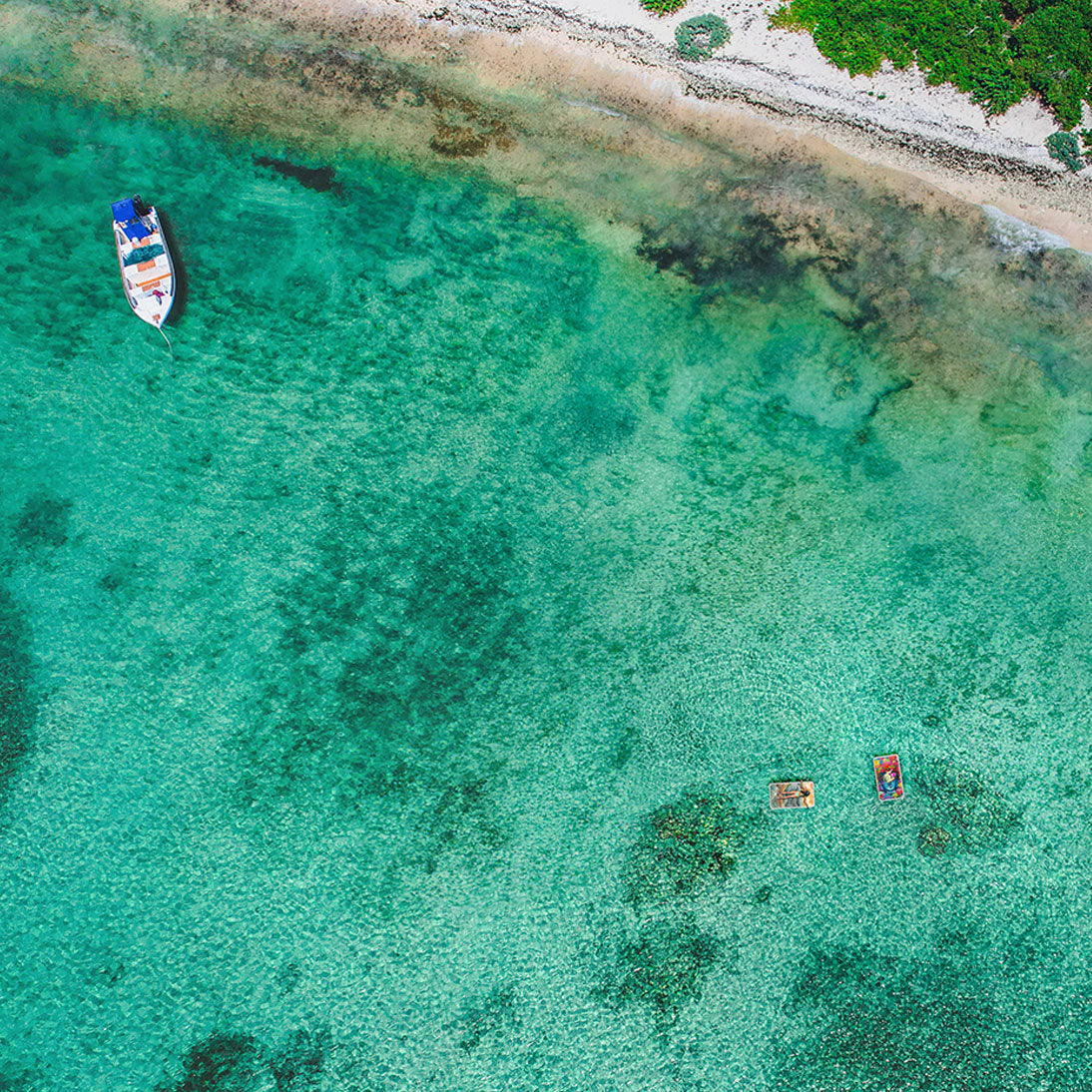 Two inflatable platforms floating on the ocean with people sunbathing next to an anchored boat