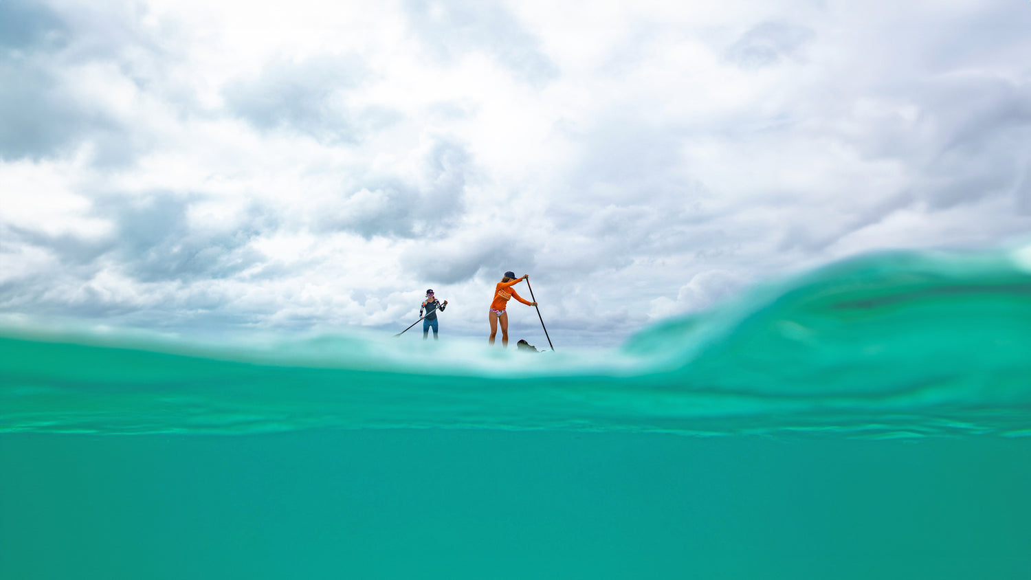 two people paddleboarding on the turquoise sea with cloudy skys