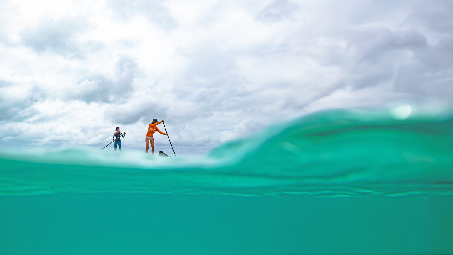 two people paddleboarding on the turquoise sea with cloudy skys above