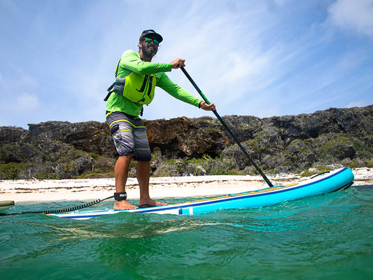 a man paddling an inflatable paddleboard past a white sandy beach having fun