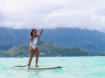 a woman paddle boarding on a bright blue ocean with mountains in the background