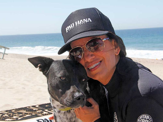 A woman with her dog on the beach with the Oahu paddleboard in the background