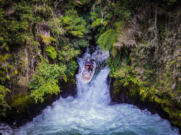 a giant SUP going over a waterfall in new zealand surrounded by native bush 