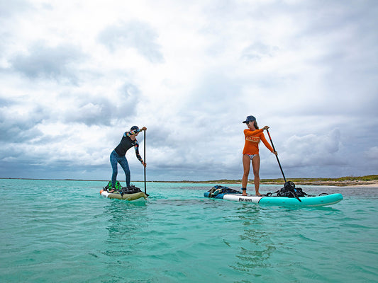 two people paddle boarding on a bright blue ocean talking to each other