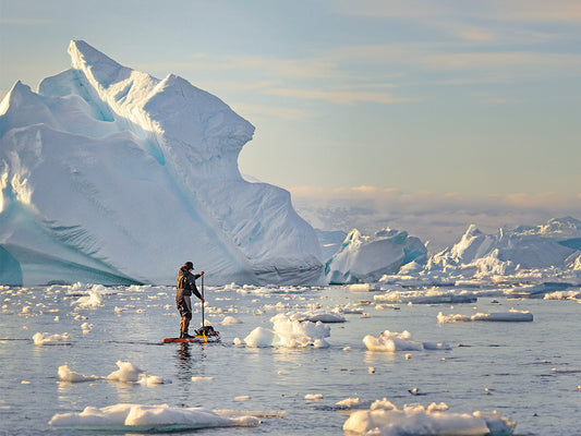 a paddle boarder paddling between iceburgs in cold conditions