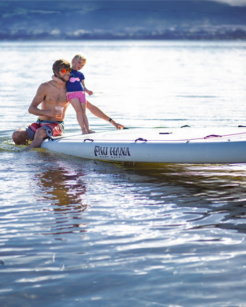 a man ans child on a big inflatable paddle board on a lake in new zealand smiling and having fun