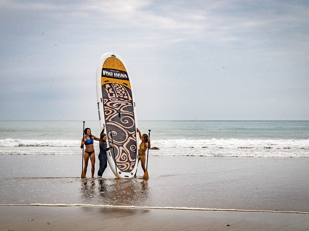 Three people on a beach with a large paddleboard featuring a design.