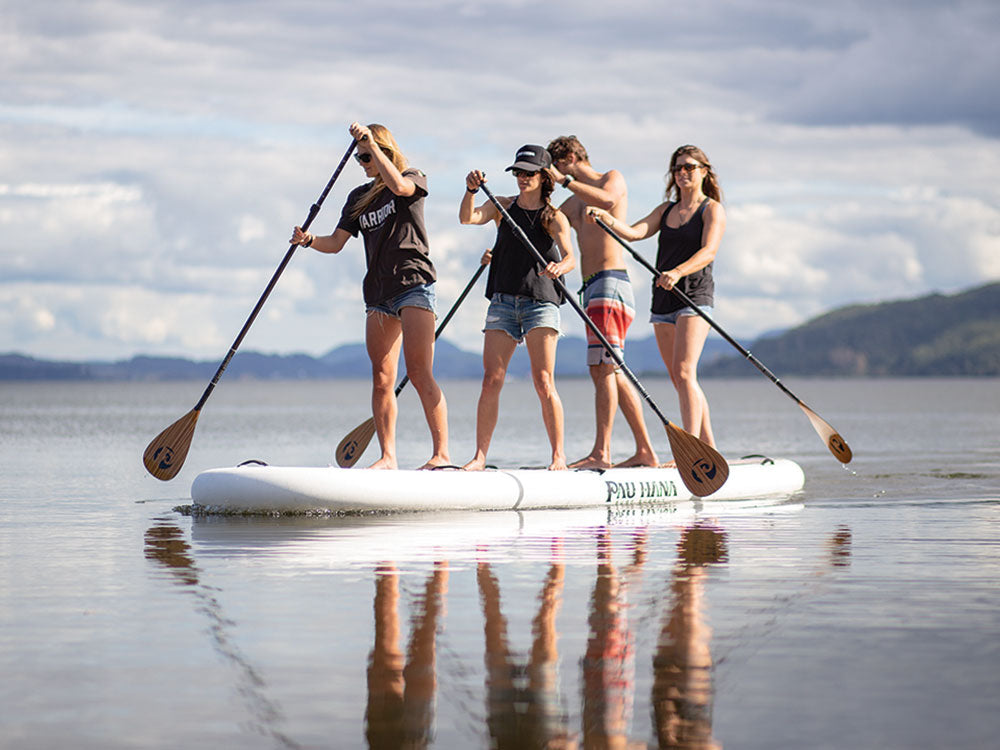 Four people paddleboarding on a calm body of water with mountains in the background.