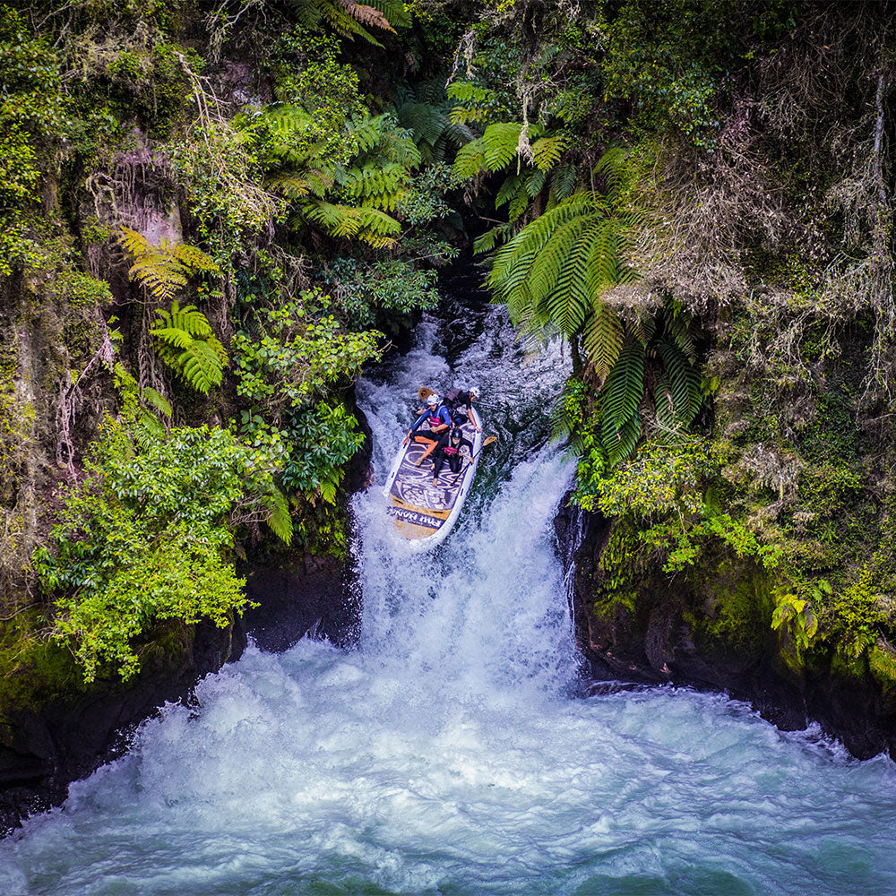 a giant inflatable paddleboard going over a waterfall on the kiatuna river in new zealand surraounded by native bush