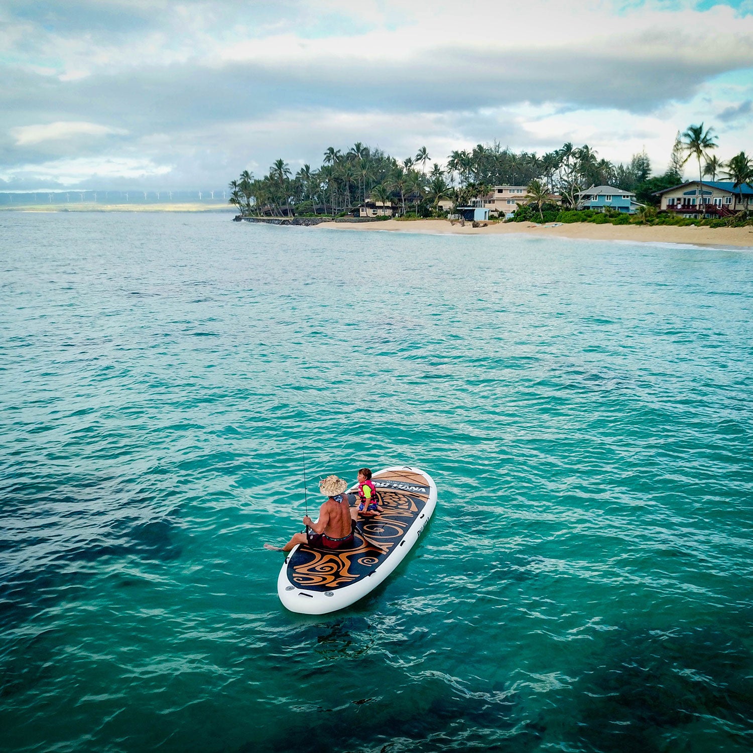 Two people on a paddleboard in the middle of a clear blue ocean with a tropical island in the background.