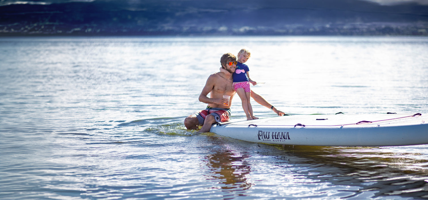 a man and child on a giant inflatable paddleboard on a lake in new zealand smiling and having fun