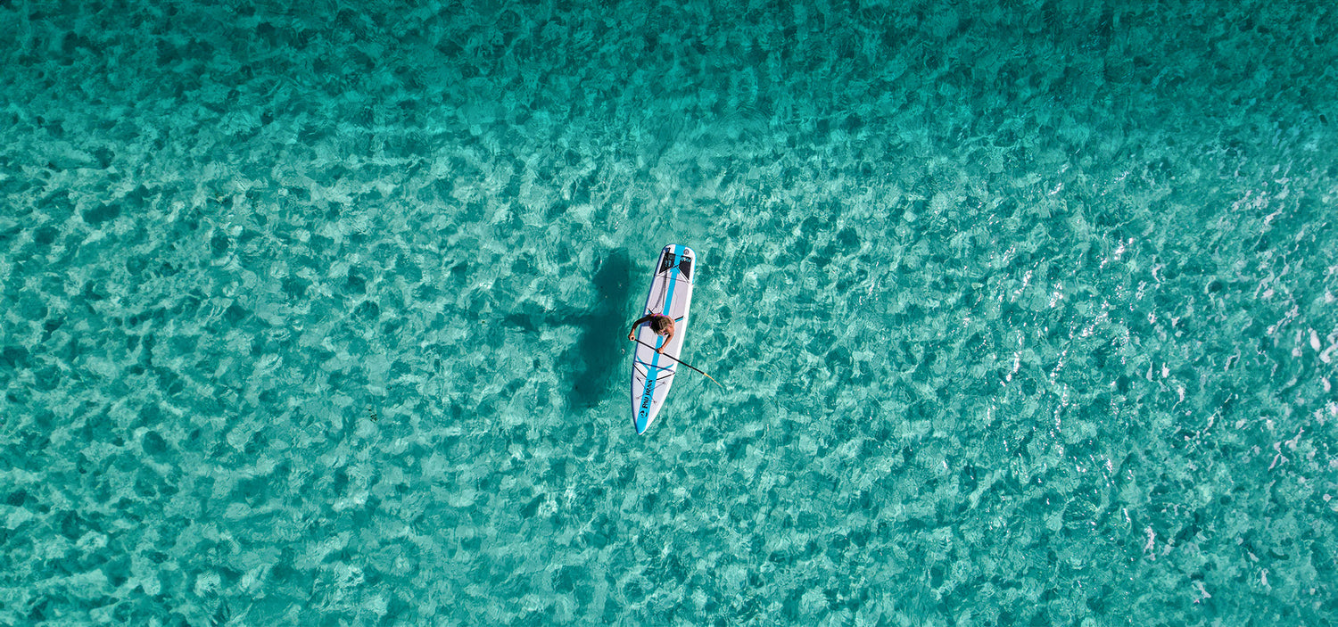 an aerial image of a paddle board being paddled on crystal clear waters