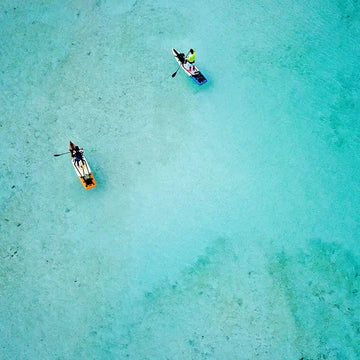 Two people paddleboarding in clear turquoise water from an aerial perspective