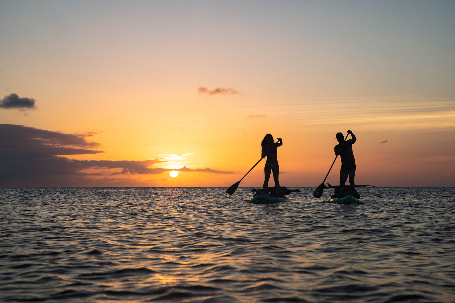 two paddleboarders at sunset paddling into the distance