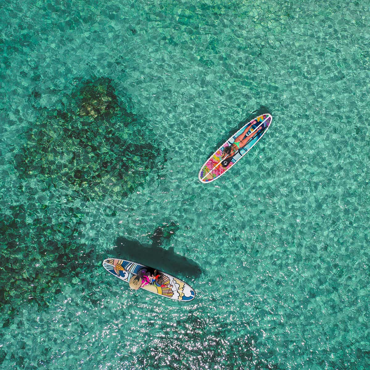 an aerial  image of two colorful paddleboarder floating on the bright turquoise sea