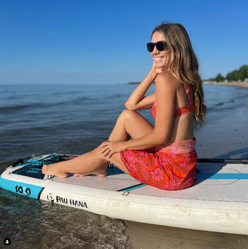 Woman in a red dress sitting on a paddleboard by the water