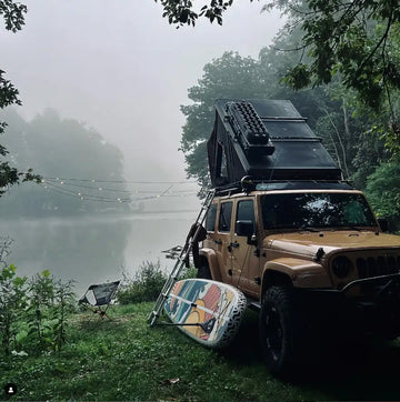Jeep with rooftop tent and inflatable paddleboard by a lake on a foggy day