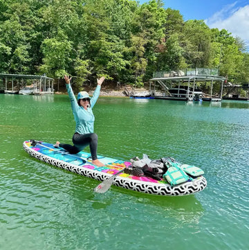 Person on a colorful stand-up paddleboard in a lake with trees and docks in the background