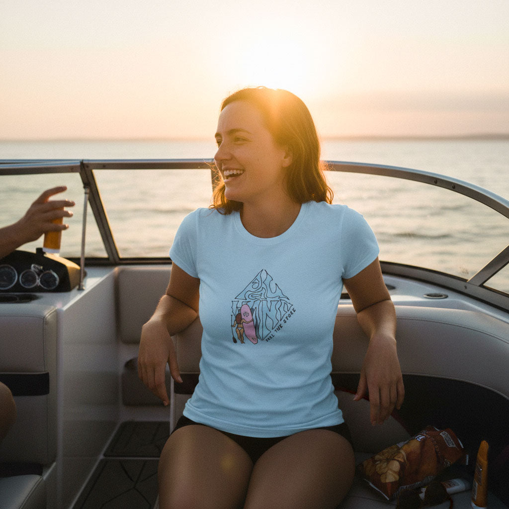 Woman on a boat at sunset wearing a light blue t-shirt with a graphic design.