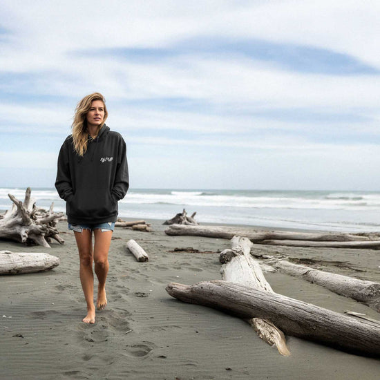 Woman walking on a beach with driftwood and ocean waves in the background
