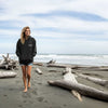 Woman walking on a beach with driftwood and ocean waves in the background
