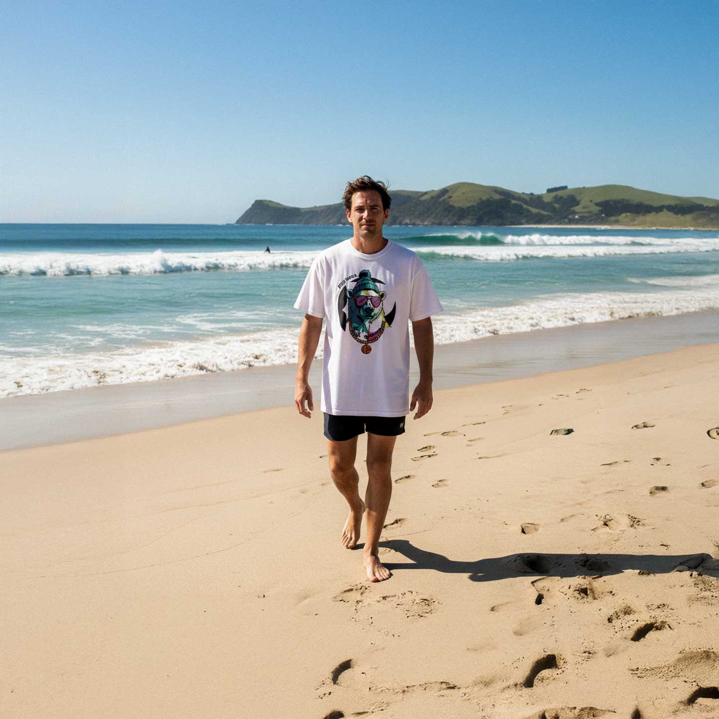 Man walking on a sandy beach with ocean and mountains in the background