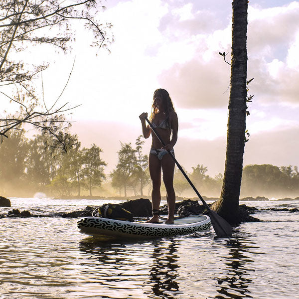 a woman paddling an inflatable paddleboard with trees and mist in the background at sunset